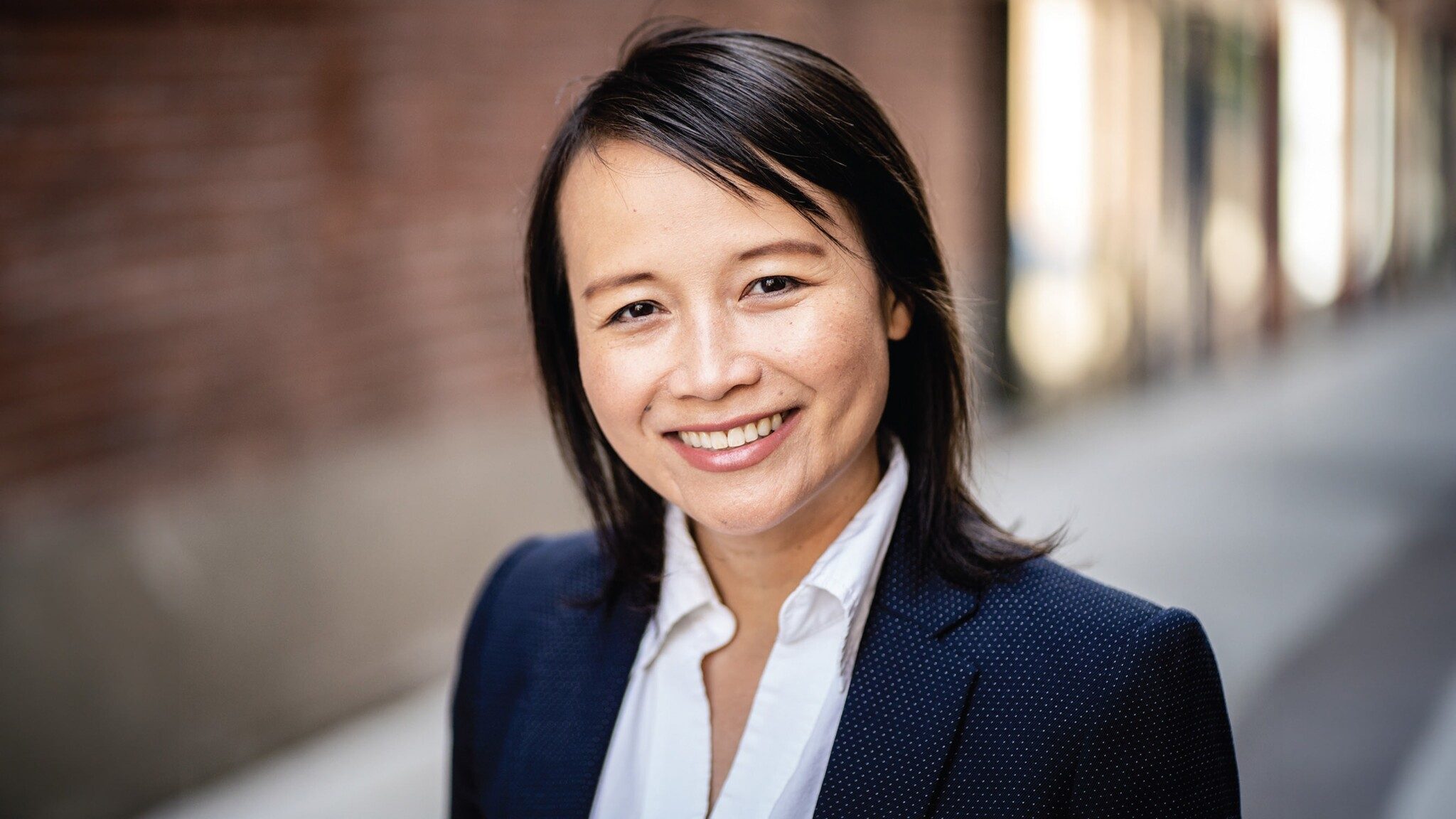 Smiling asian woman in a business suit standing against a blurred urban background.