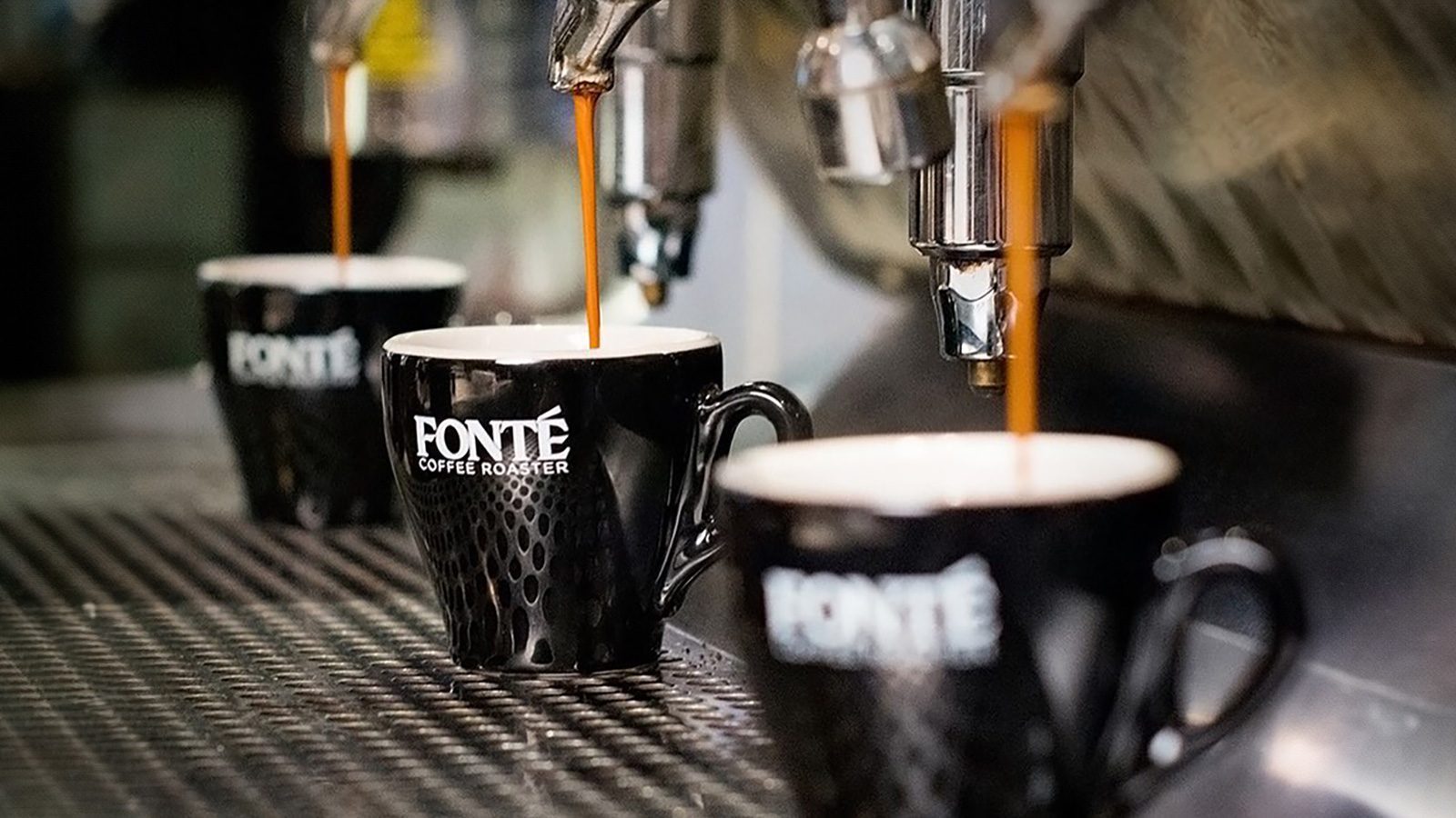 Three black Fonte coffee mugs are placed under espresso machines with espresso being dispensed into them, creating a scene of artisanal coffee art.
