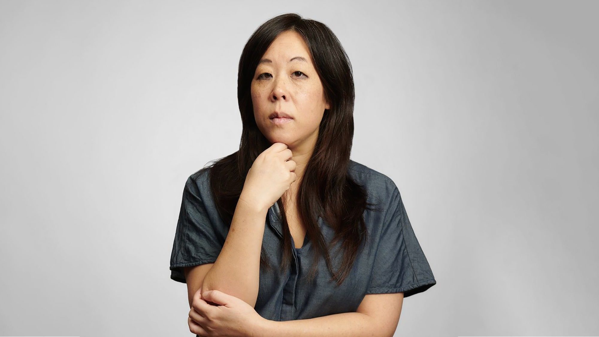 Portrait of a middle-aged asian woman with a contemplative expression, resting her chin on her hand.