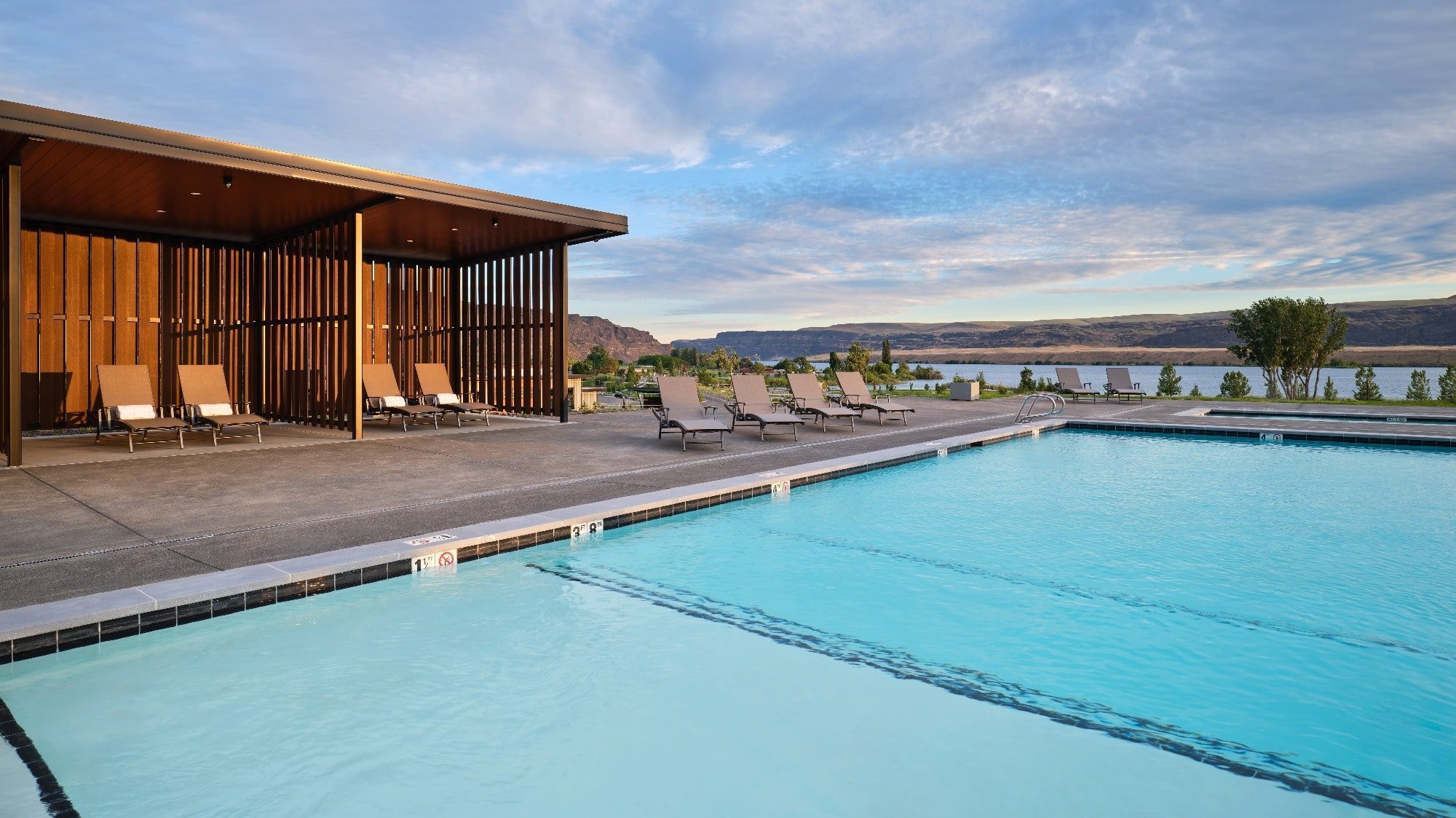 Outdoor swimming pool with lounge chairs and a wooden cabana on a clear day, overlooking the scenic landscape of Crescent Ridge with hills and water in the background, highlighting the premium amenities of this winery venue.