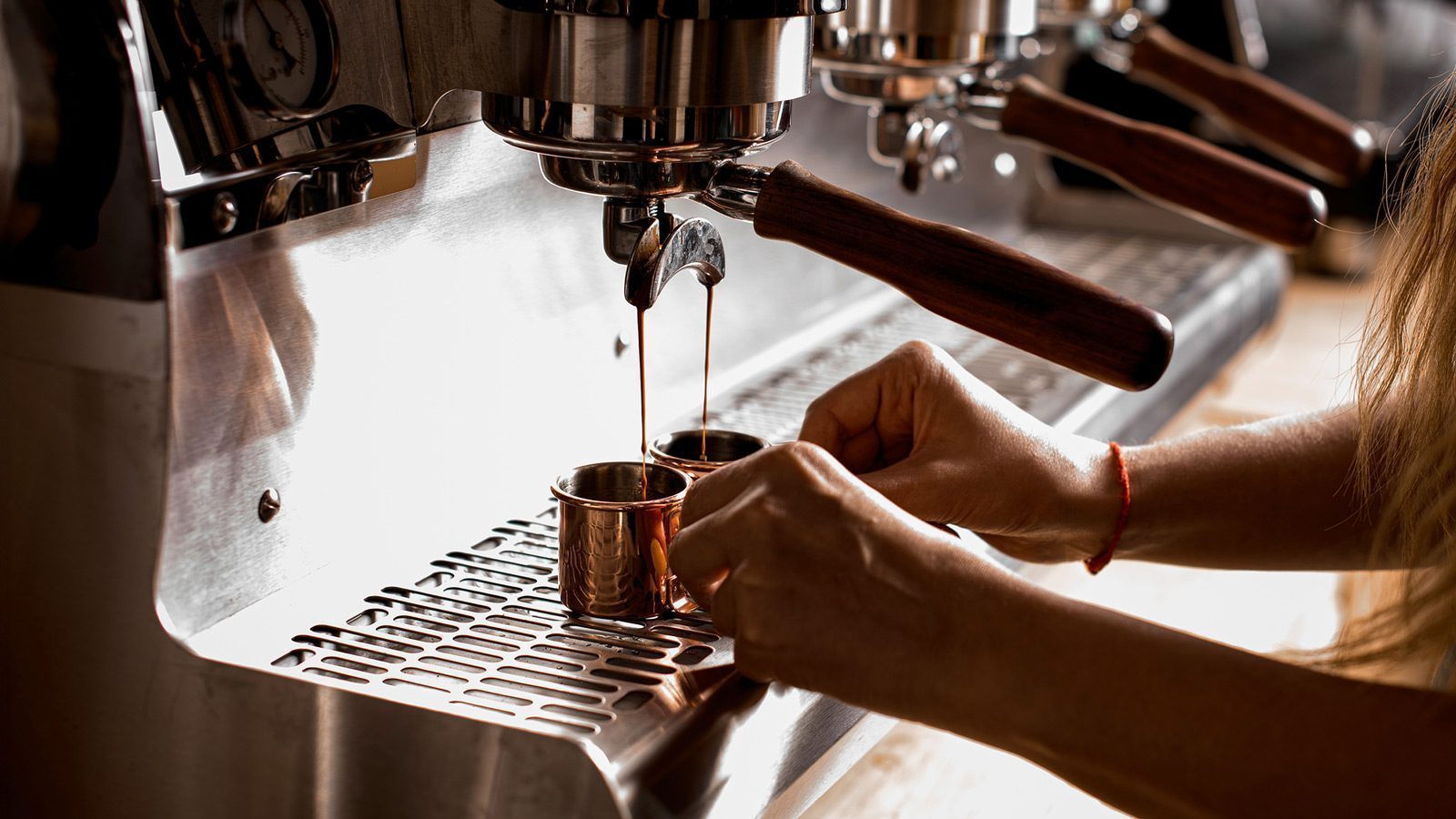 From the perspective of a seasoned barista in Seattle, a person skillfully makes espresso on a commercial coffee machine, with two streams of rich coffee filling small cups.