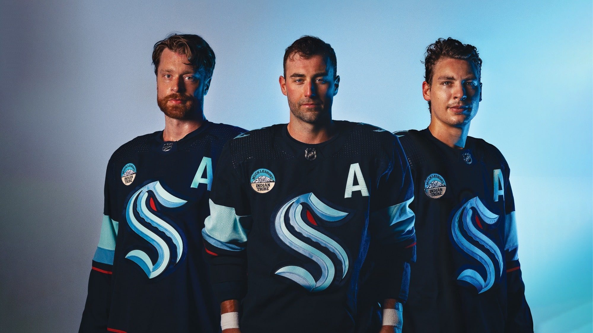 Three hockey players in navy blue uniforms, each with an "A" on their jerseys, stand in a row against a blue gradient background, epitomizing the pride of sports franchises jerseys that jersey fans admire.