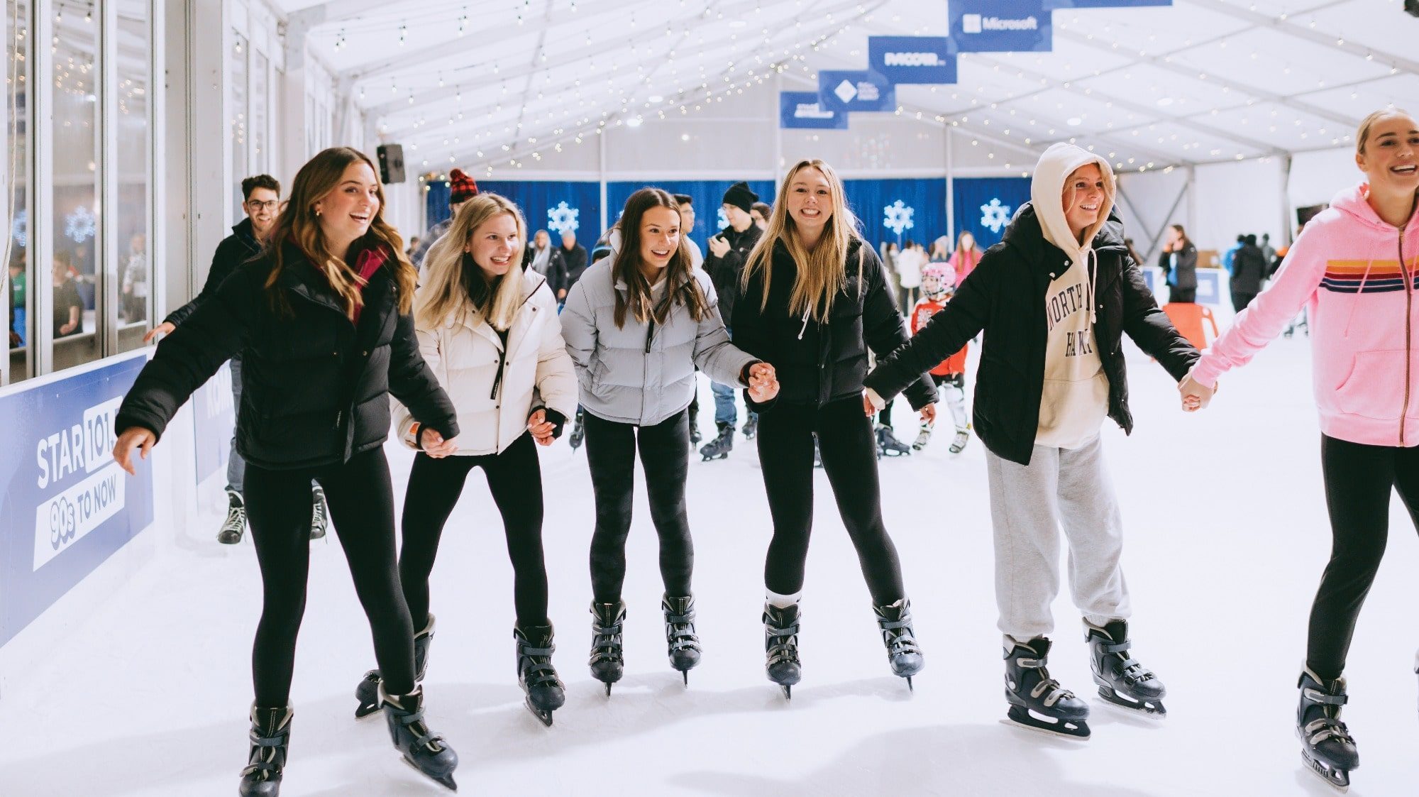 A group of six people enjoy ice skating indoors, holding hands and smiling—perfect for what to do in Seattle during the holiday season.
