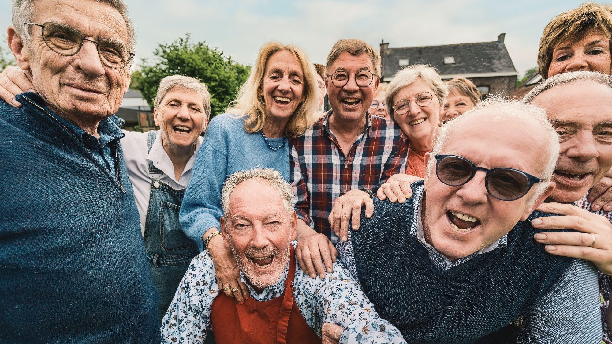 A group of older adults smiling and posing together outdoors, embodying the joy of friendship in their casual clothing.