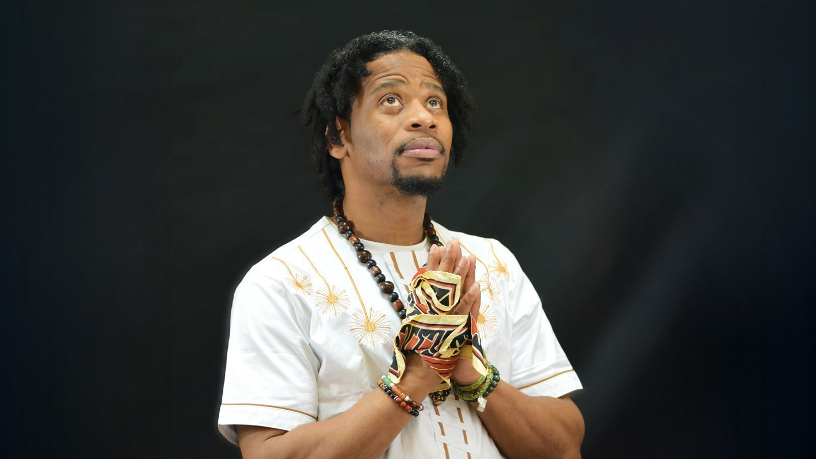 A person wearing a white embroidered shirt and patterned gloves is looking upward into the vast space, seeking a moment of healing against the dark background.