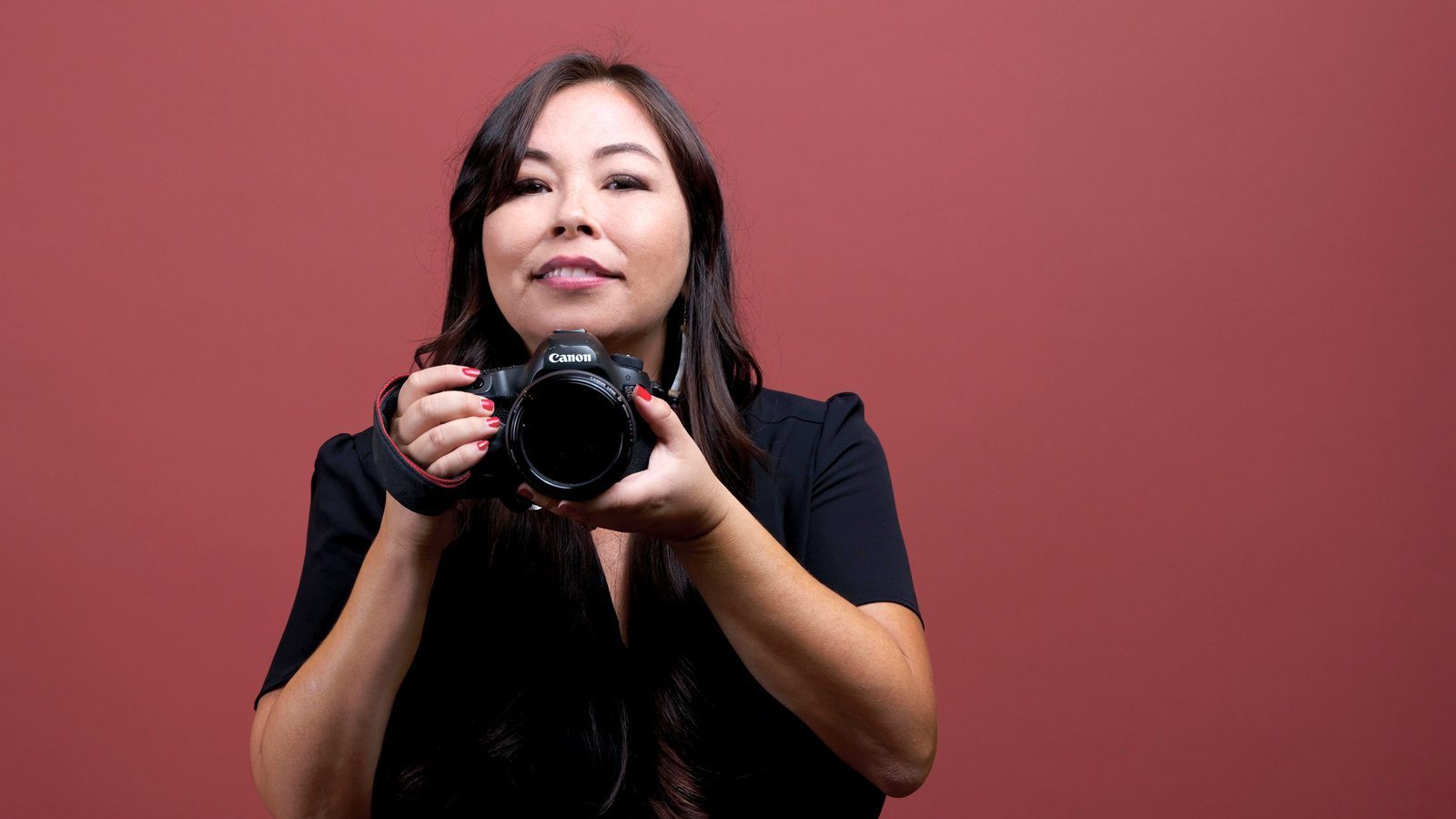 A person, reminiscent of Matika Wilbur's captivating portraits, holds a camera against a vibrant red background, their gaze meeting the viewer's eyes with an intensity that draws you in.