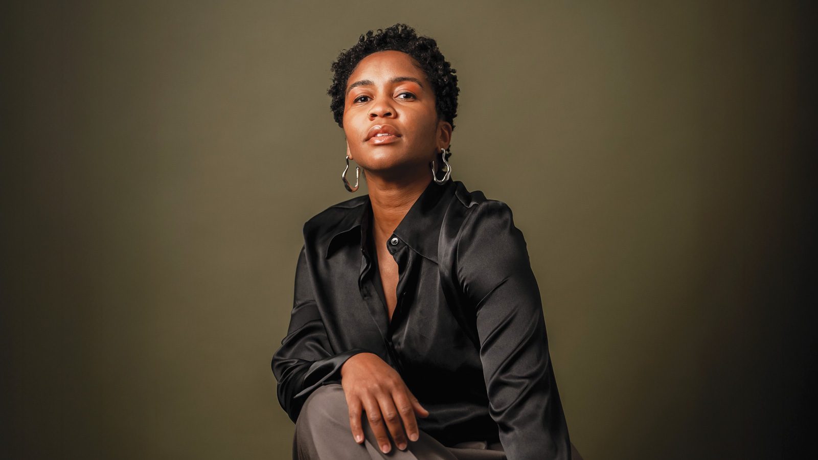 Person in a black shirt, much like dancer and choreographer Nia-Amina Minor, sits with a thoughtful expression against a plain background.