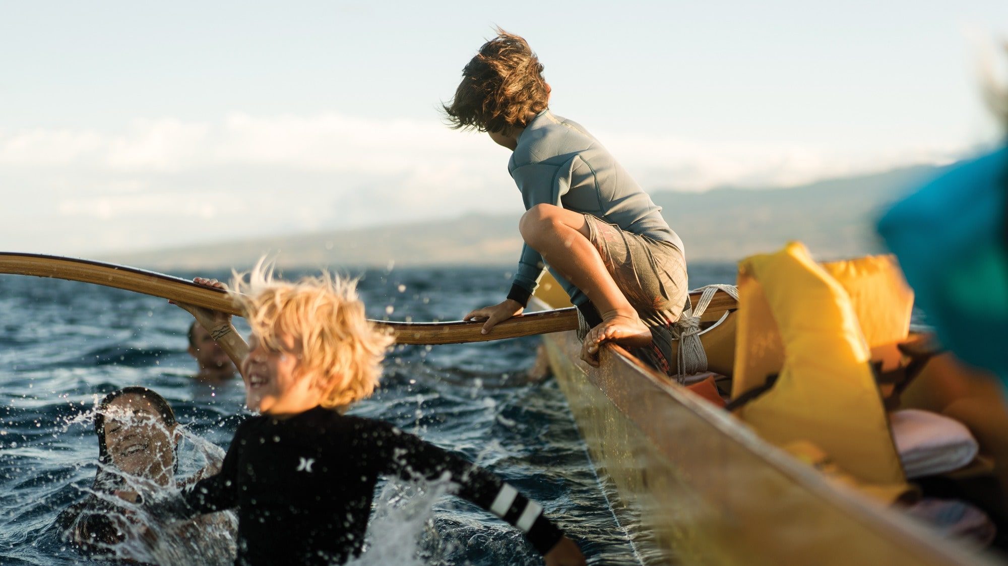 On a sunny beach, children are joyfully playing and jumping off a canoe into the sparkling ocean. One child sits at the edge, soaking in the warmth, while others splash happily in their lively vacation adventure.