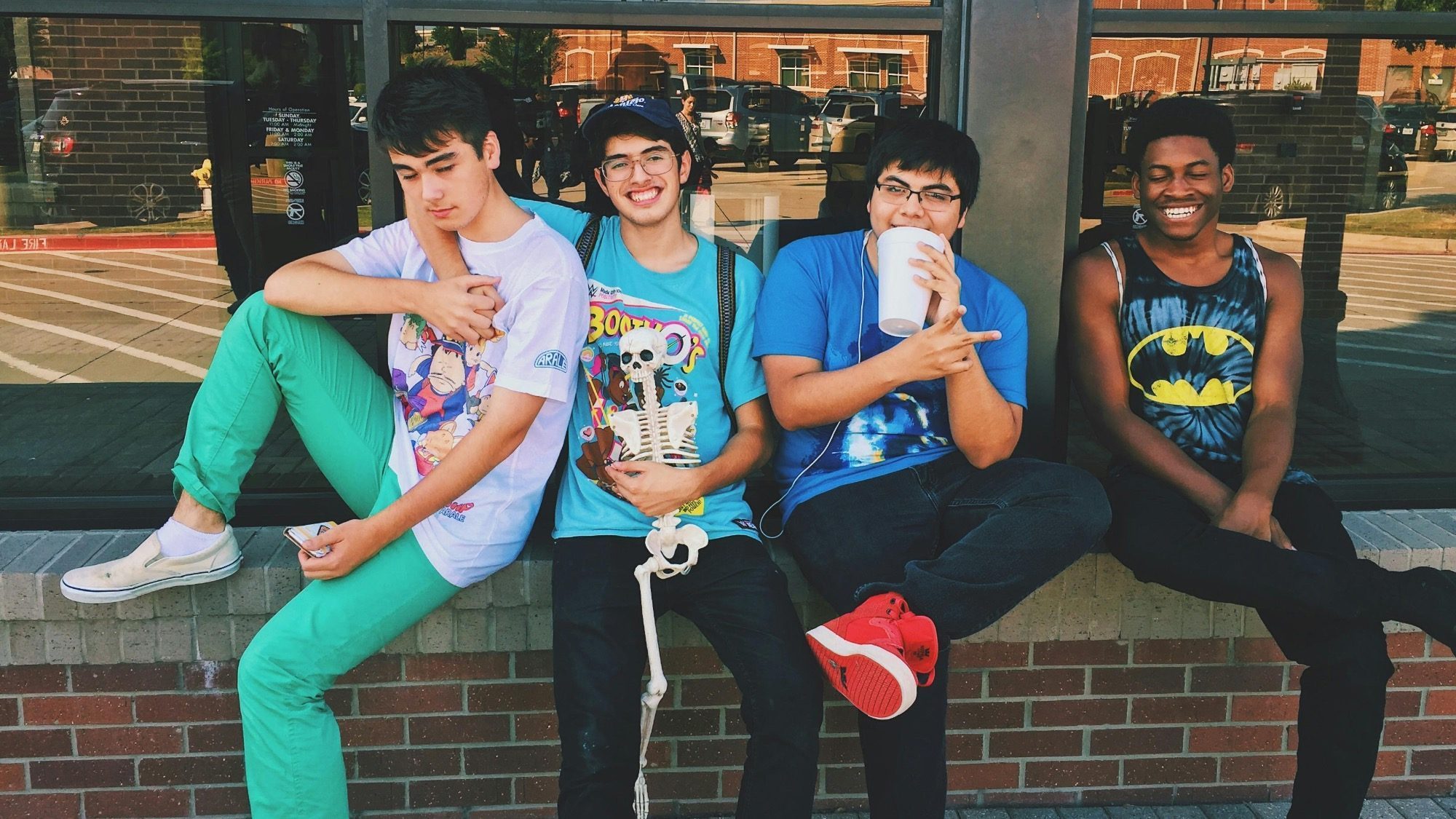 Four teens sit and stand by a brick wall in Seattle, smiling and holding drinks. They wear casual, colorful outfits and seem relaxed and happy, perhaps sharing stories about their latest adventures or discussing the benefits of free virtual therapy.