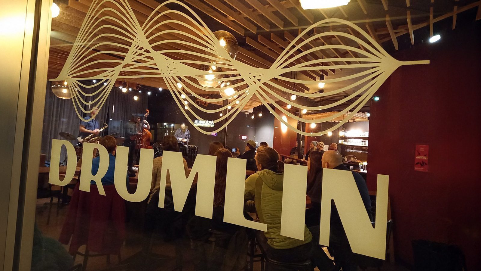 Peering through the window marked "Drumlin," the dimly lit interior reveals a space that has reinvented itself, with people seated and a band playing evocatively on stage.