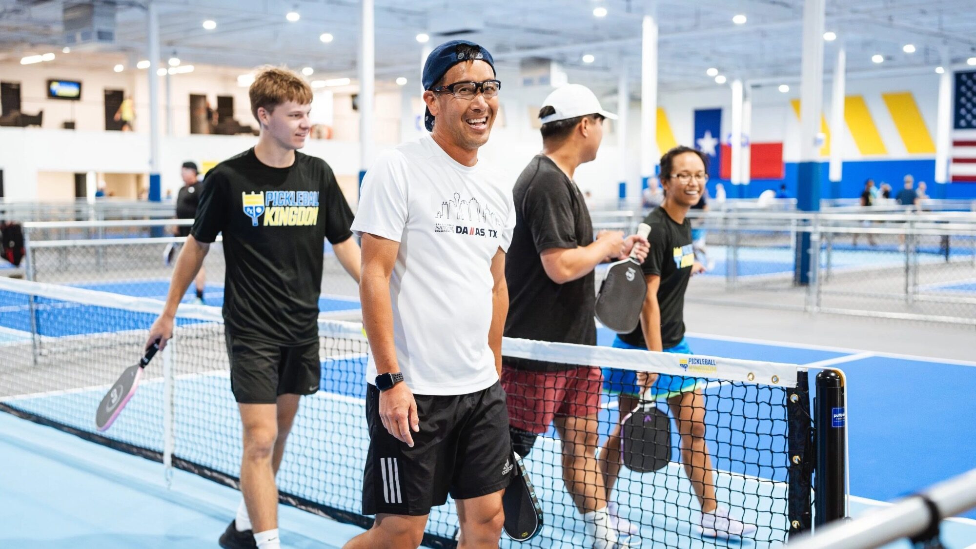In a lively frenzy, four people holding pickleball paddles walk on an indoor court in Poulsbo, smiling and chatting.