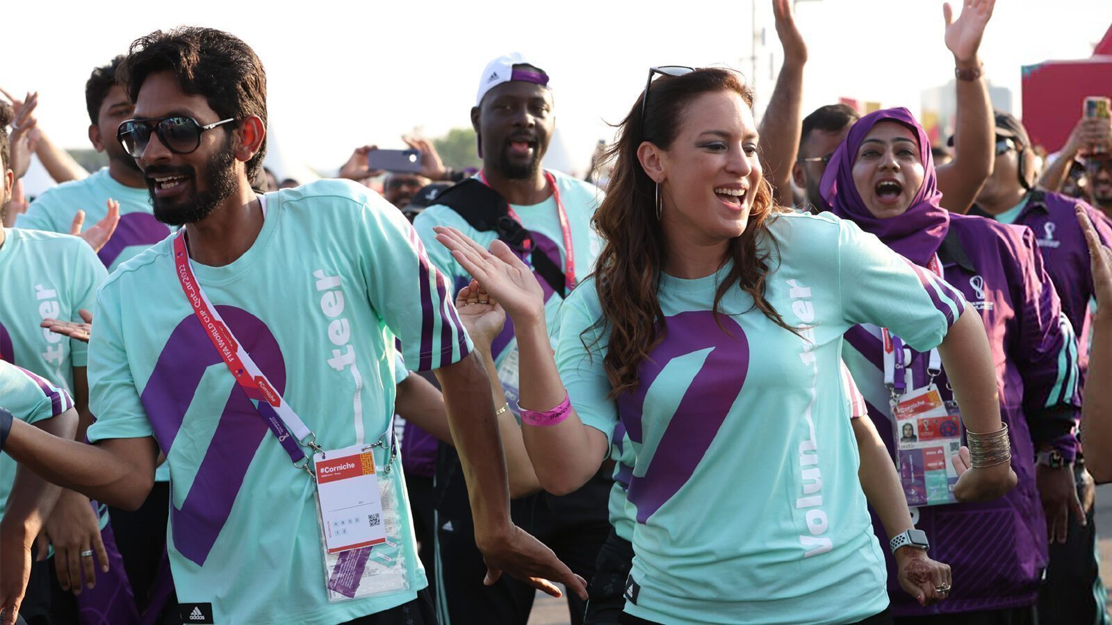 A group of volunteers in matching shirts dance and smile outdoors, participating in a lively event.