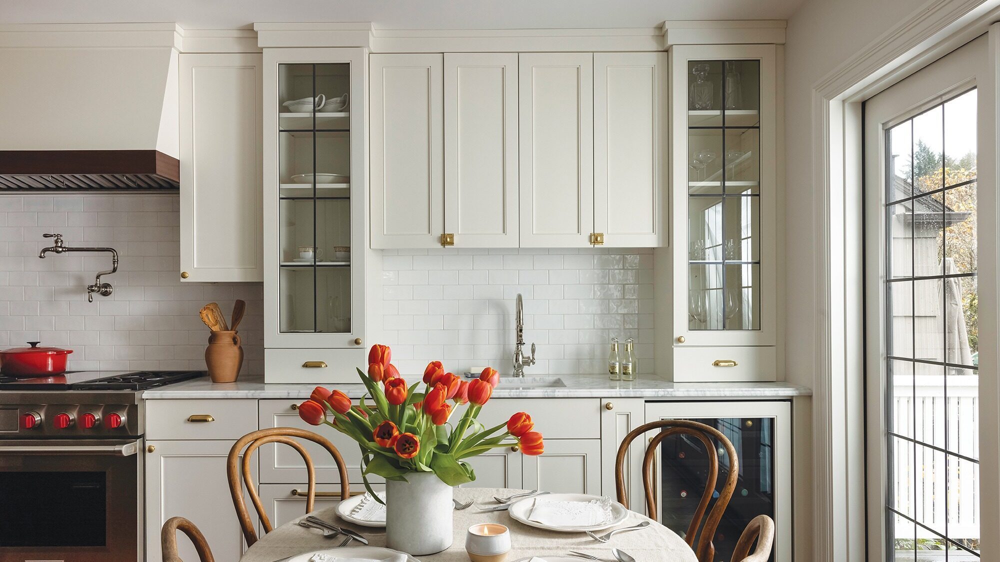 A bright kitchen with white cabinets, a table set for four, a vase of red tulips, and large windows letting in natural light—classic charm of living in Montlake and its historic Tudor homes.