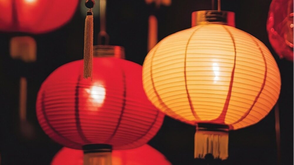 Close-up of illuminated red and yellow paper lanterns hanging against a dark background, evoking the ambiance of a memorable meal during a culinary getaway in British Columbia.