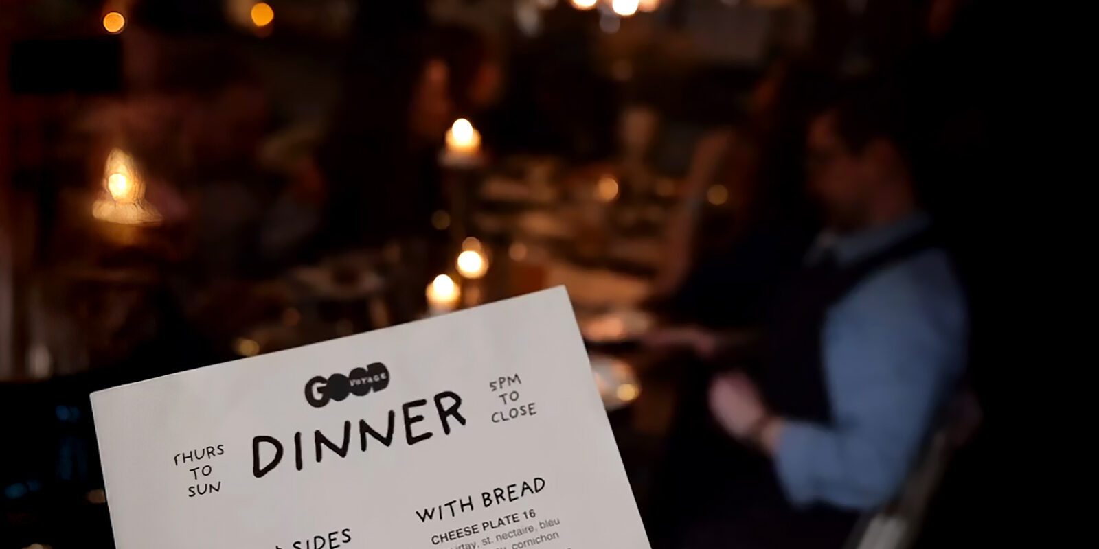 A close-up of a dinner menu held up in a dimly lit restaurant during Panda Fest, with blurred patrons and candlelit tables in the background.