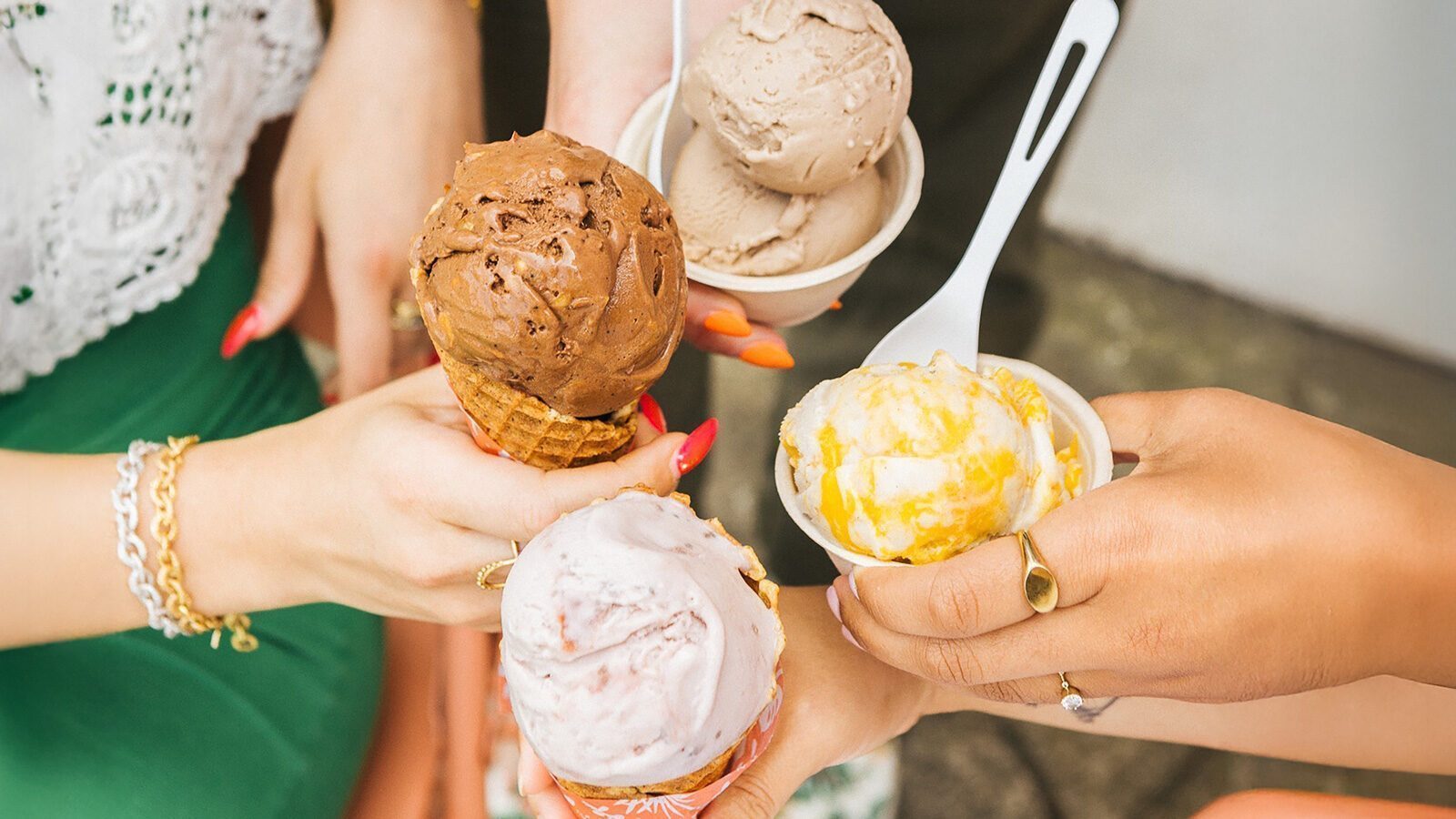 Four hands holding different flavors of ice cream in cones and cups, photographed from above, capture a moment of Sweet Relief on a warm day.