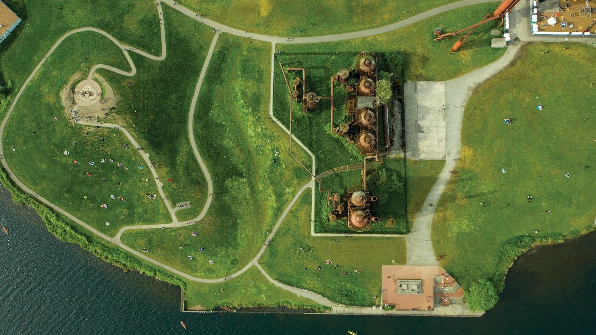 Aerial view of Gas Works Park in Seattle, one of the top Seattle parks, showing pathways, grassy areas with people, water, and the historic gas plant structures.