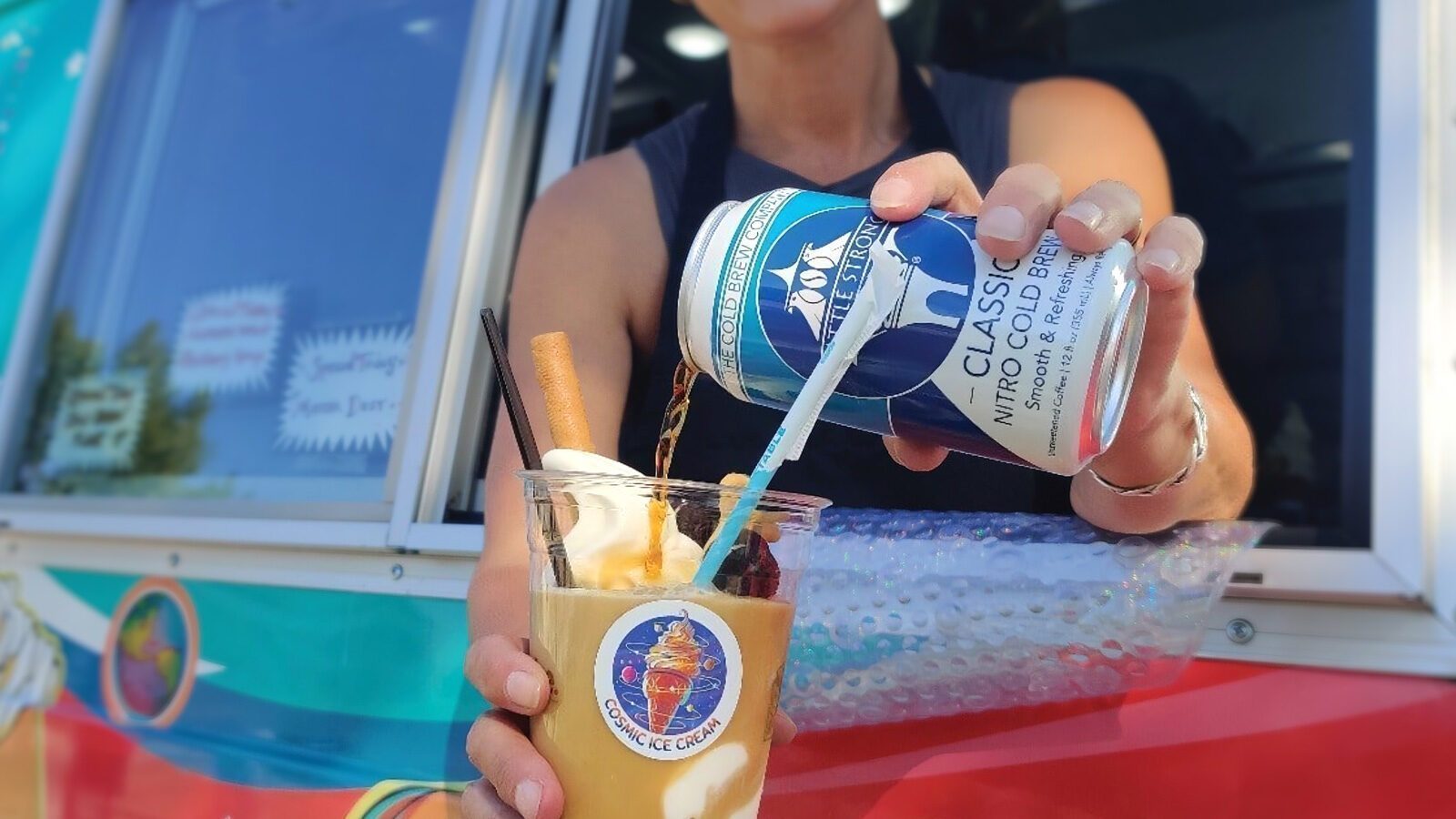 Person pouring nitro cold brew coffee from a can into a plastic cup with soft serve ice cream and a straw, in front of a colorful food truck window—a perfect treat after exploring Seattle restaurant roundup features a coffee showdown.