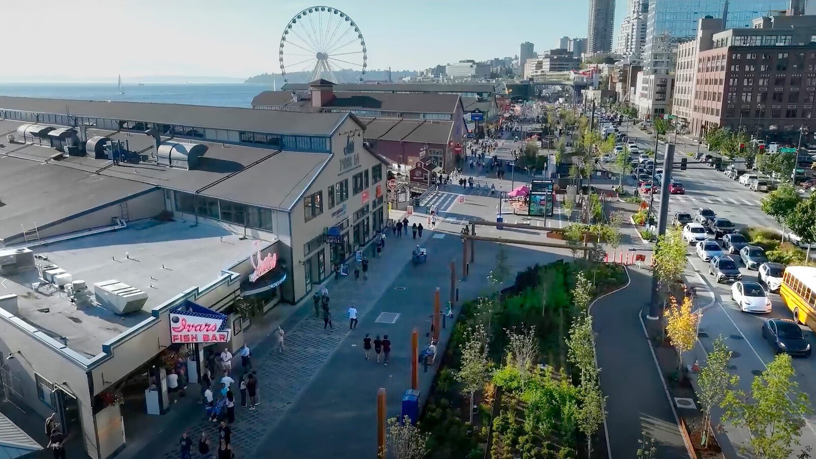 Aerial view of a busy Seattle waterfront area with people walking, green landscaping, a large building, and a Ferris wheel by the water—showcasing this vibrant U.S. walkable city.