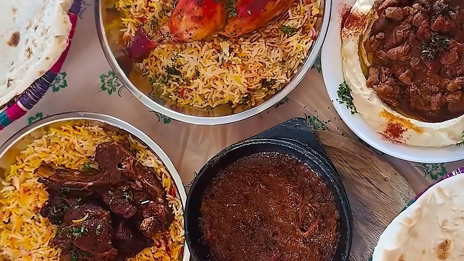 An overhead view of various Middle Eastern dishes—rice with lamb shank, braised meat, and flatbread—arranged on a table, perfect for seasonal eating and enjoying August foods.