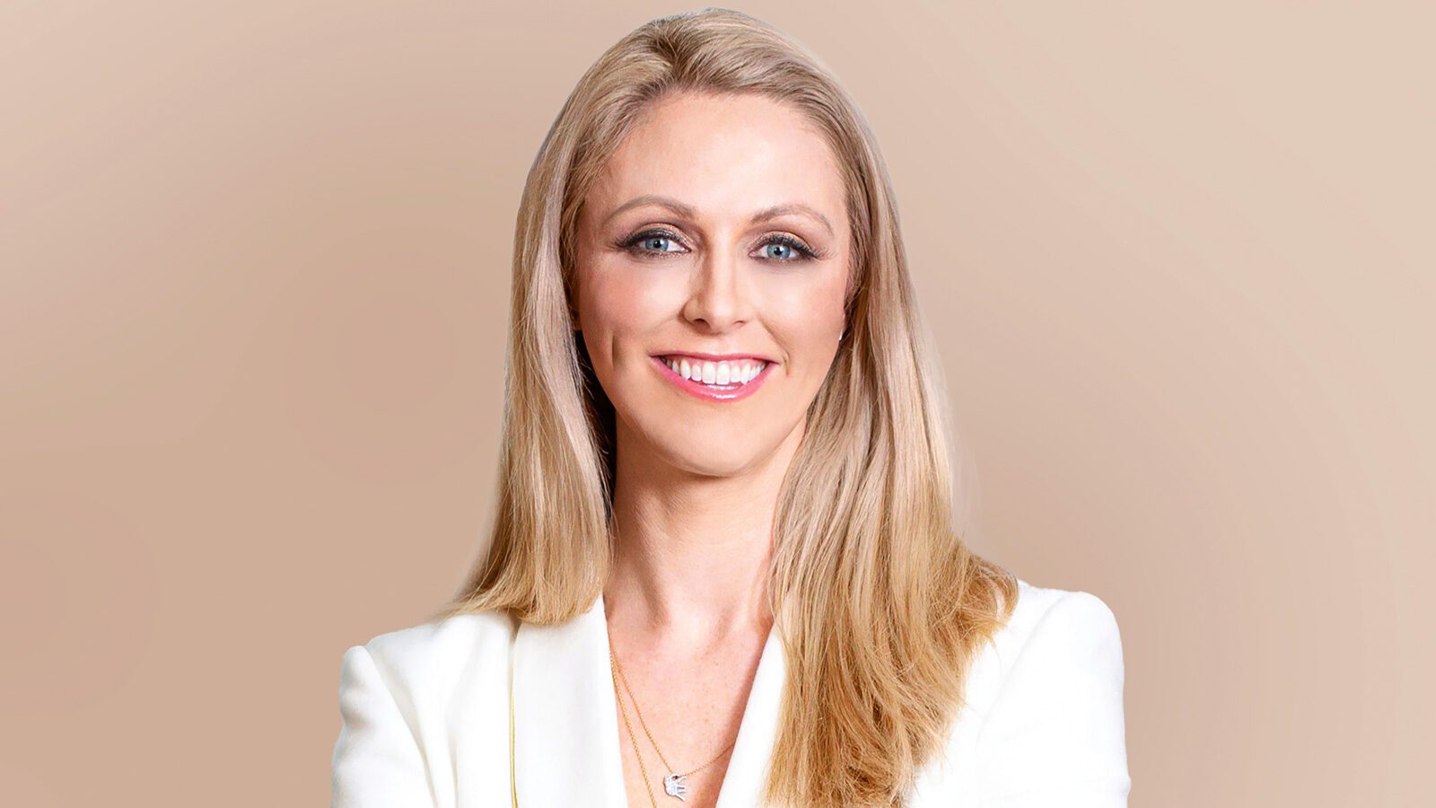 Dr. Meghan Nadeau, a woman with long blonde hair, wears a white blazer and a necklace, smiling at the camera against a plain beige background.