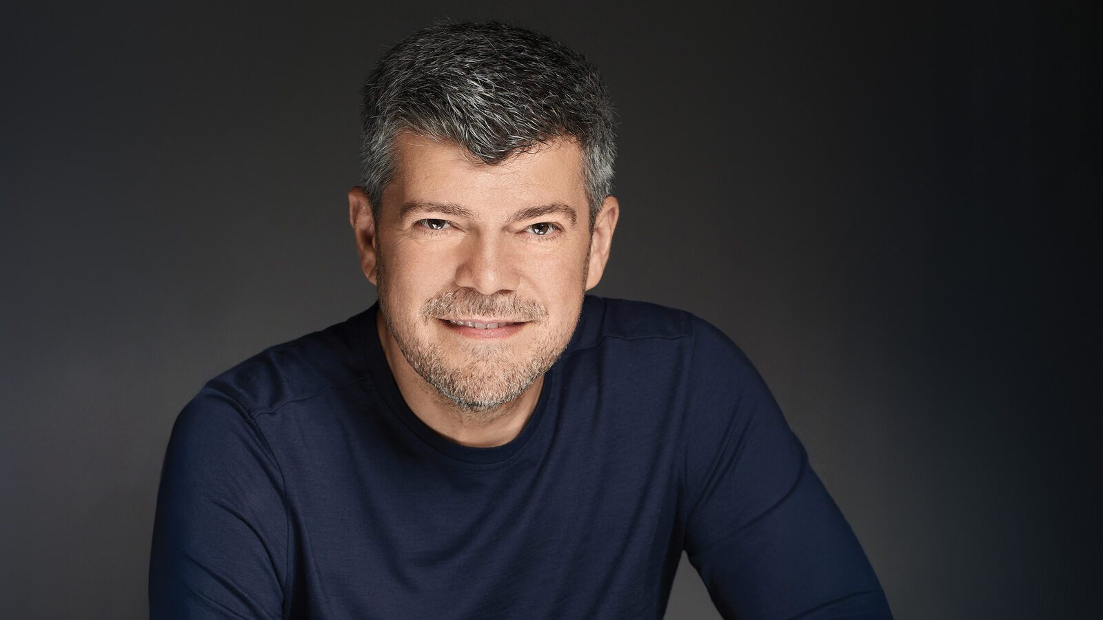 Dr. Nicolae Leca, M.D., a middle-aged man with short gray hair and a trimmed beard, is smiling and wearing a navy blue shirt against a plain dark background.
