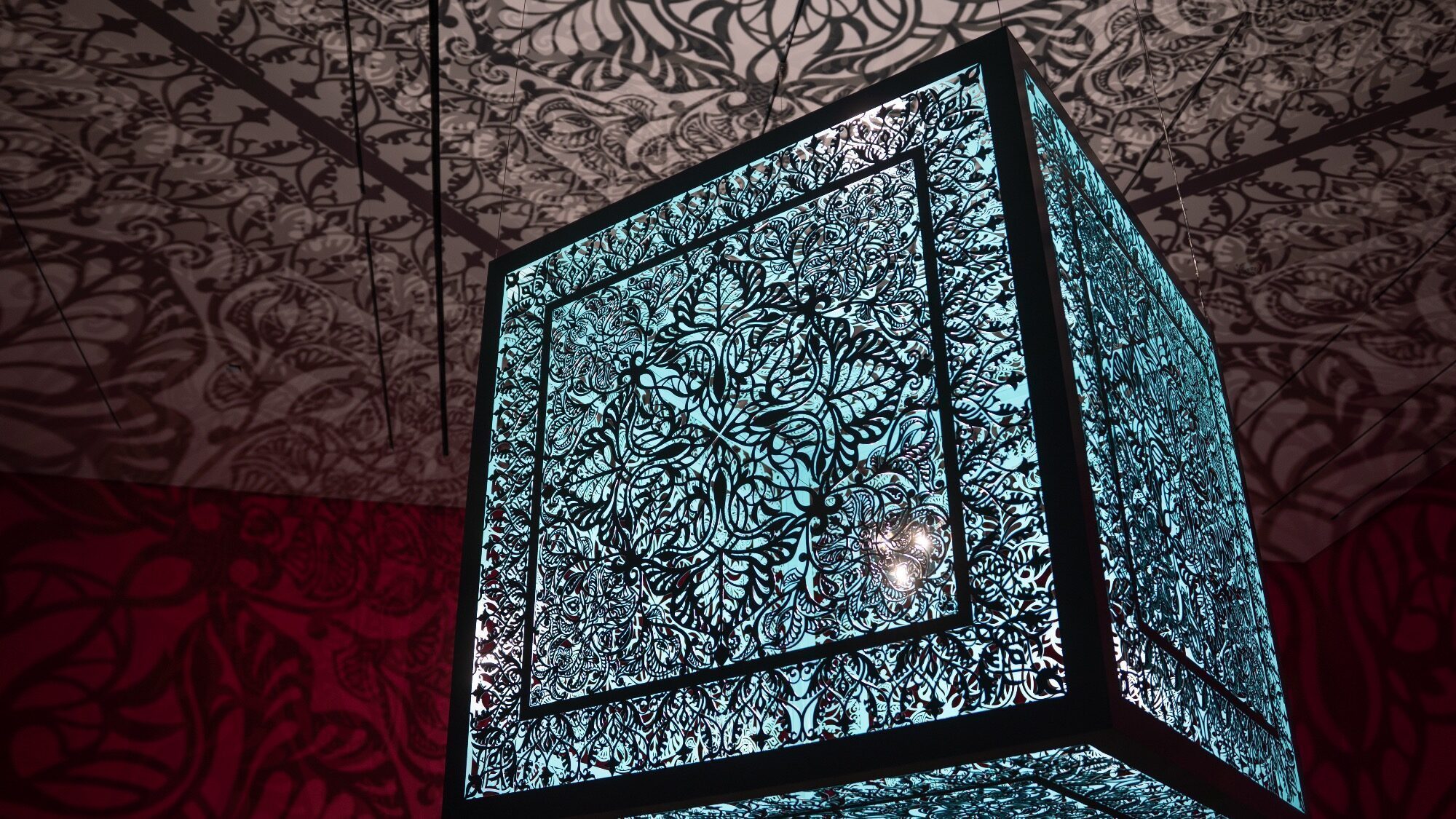 A decorative cube-shaped light fixture with intricate floral cut-out patterns casts detailed shadows on the ceiling and walls.