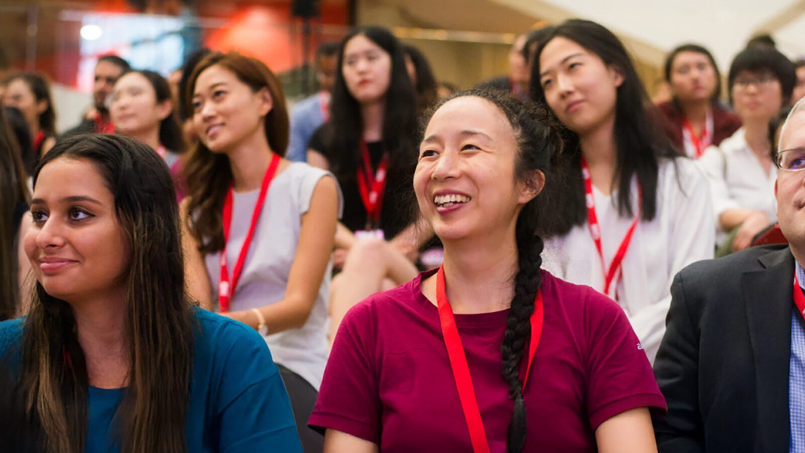 A group of people wearing red lanyards sit together indoors, smiling and listening attentively during an AAJA event or Back to the Future-themed presentation.