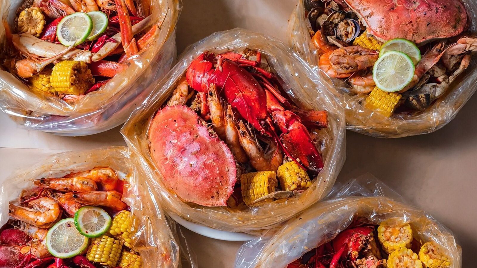 Four bags filled with assorted seafood, corn, and sliced lime are displayed on a table—a true Shilshole Seafood Boil highlight for any Underground Eats adventure.
