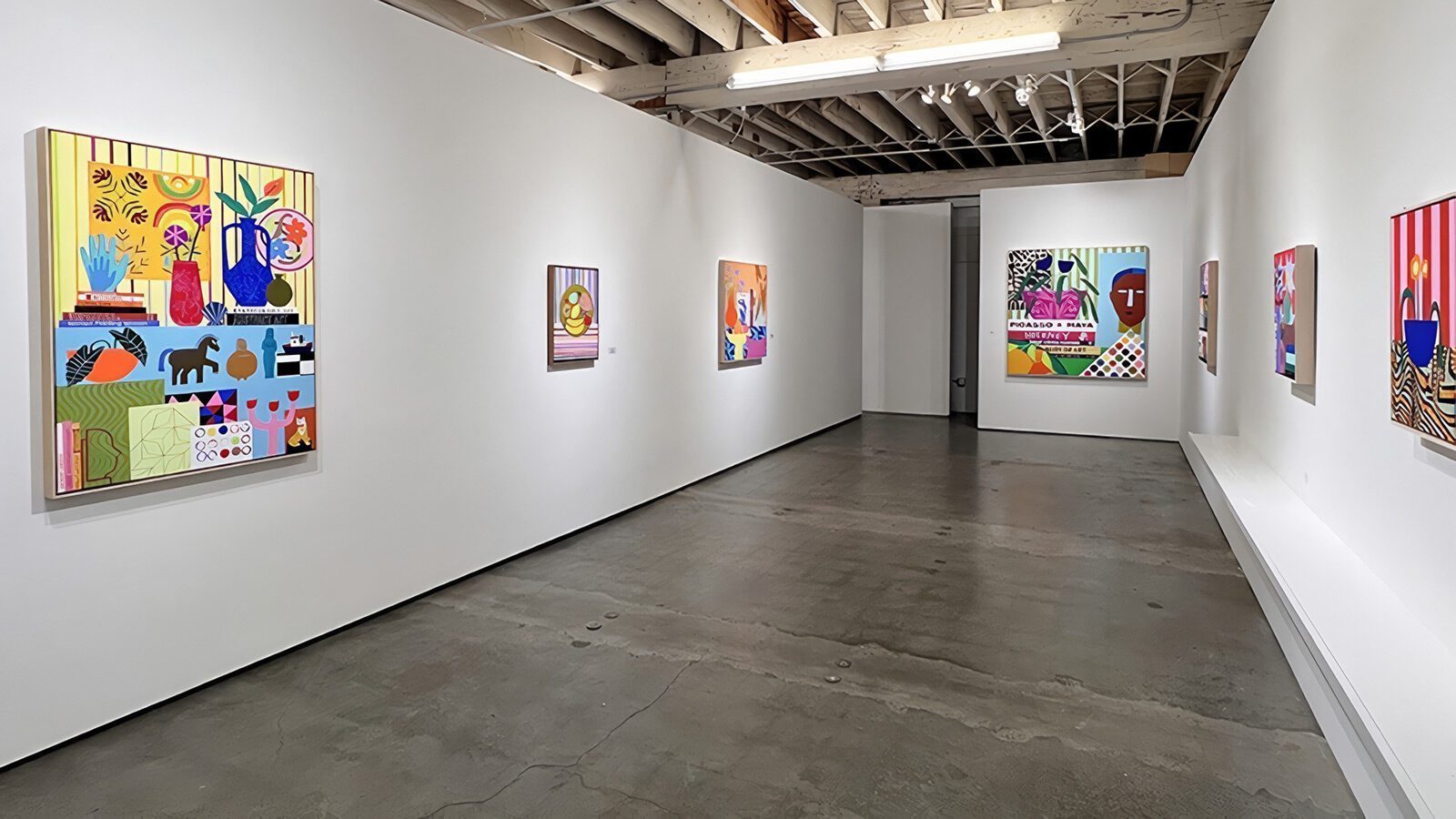 Art gallery interior with white walls displaying colorful, modern paintings—an inviting spot for visual arts enthusiasts; polished concrete floor and exposed wooden ceiling beams complete this must-see Seattle arts destination.