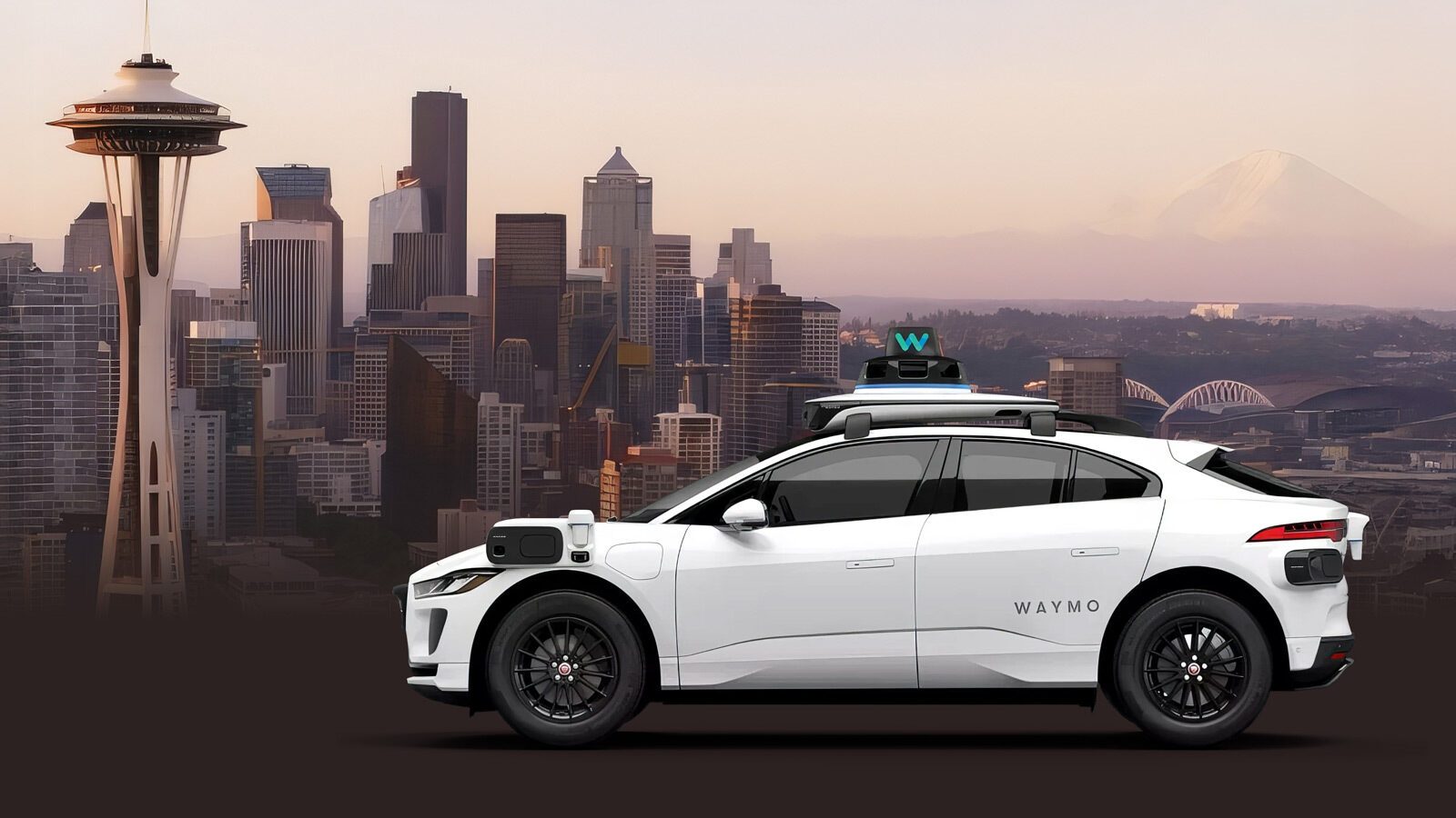 A white Waymo self-driving car is parked in front of the Seattle skyline, with the Space Needle and Mount Rainier visible in the background.