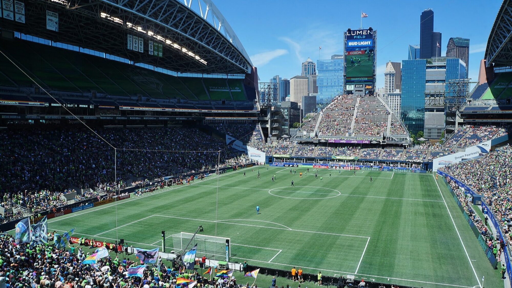 A large soccer stadium filled with fans and World Cup excitement, featuring a green field and a city skyline in the background under a clear blue sky.