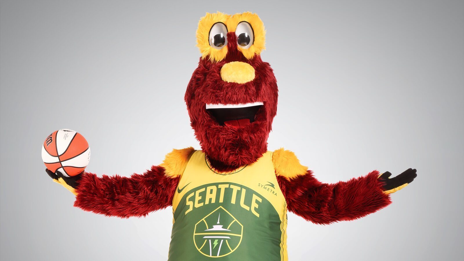 Doppler, the red and yellow furry mascot in a Seattle basketball jersey, holds a basketball in one hand and gestures with the other, showcasing his Best of the Best energy against a plain background.