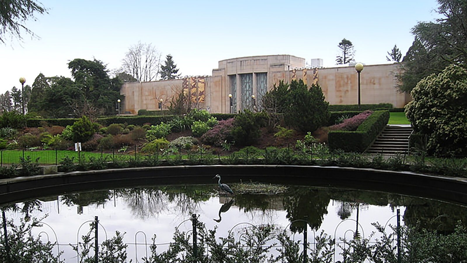 A landscaped garden with trimmed hedges and a circular pond sits in front of the Seattle Asian Art Museum, a notable Seattle landmark, on a clear day.