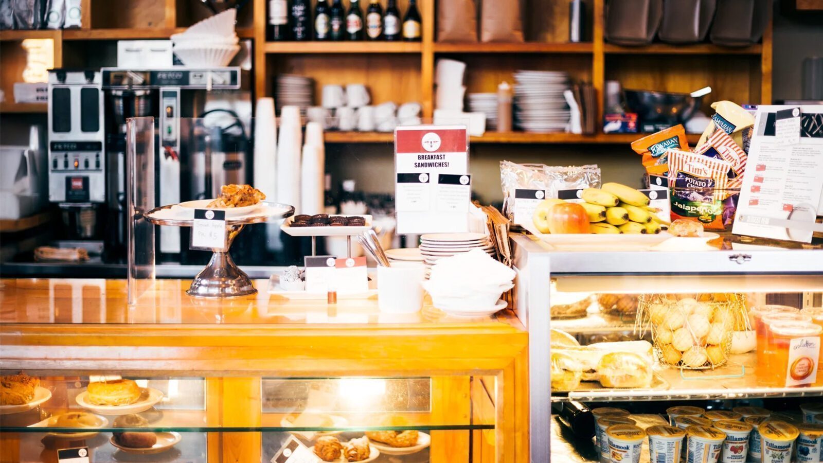 Bakery counter at Zeitgeist Coffee displaying pastries, cookies, fruit, and snacks, with shelves of cups, plates, and bottles in the background—a perfect breakfast spot at your favorite coffee shop.