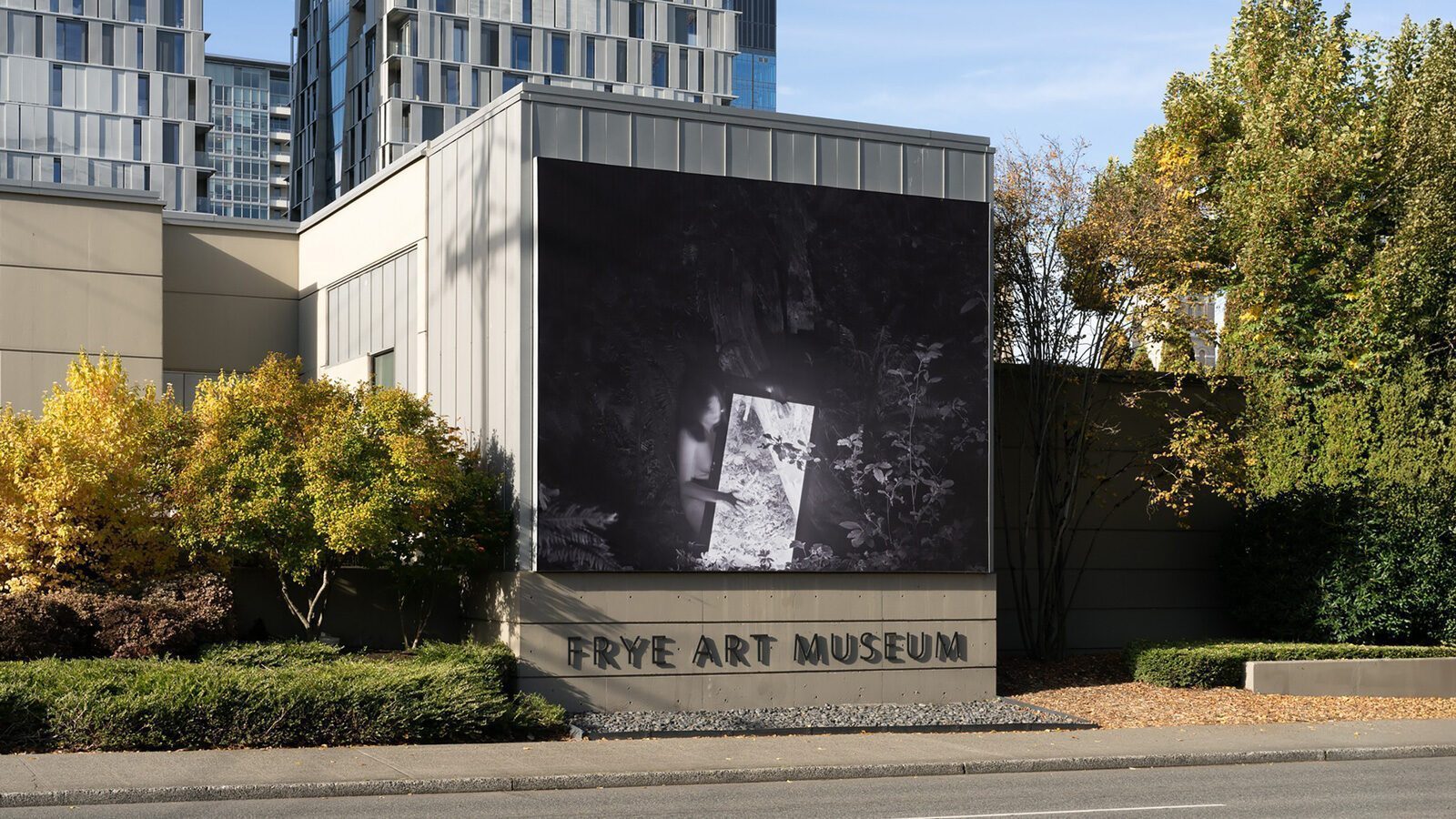 The Frye Art Museum offers free access to compelling art, with its exterior featuring a striking black-and-white photograph displayed on the building’s facade, surrounded by trees and urban buildings.