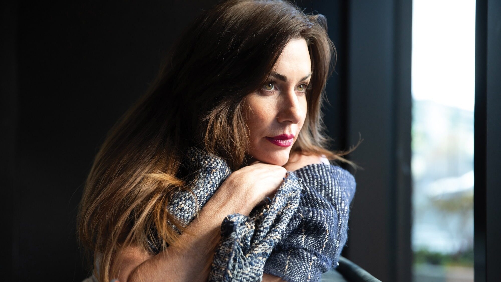 Woman with long brown hair rests her chin on her crossed arms, gazing out of a window as natural light illuminates her face, deep in thought about learning to pivot and new SBM opportunities.