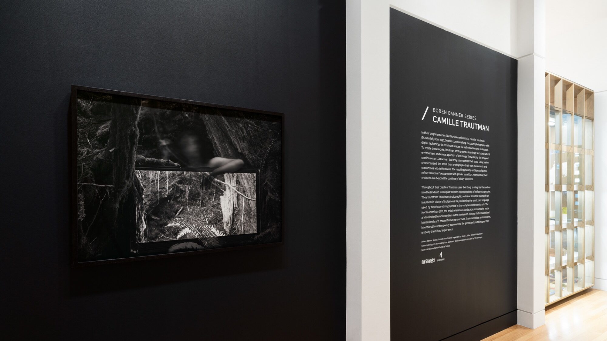 A framed black-and-white photograph hangs on a dark wall next to exhibition text about artist Camille Patha at the Frye Art Museum, showcasing the work of a talented Seattle photographer in a refined gallery space.