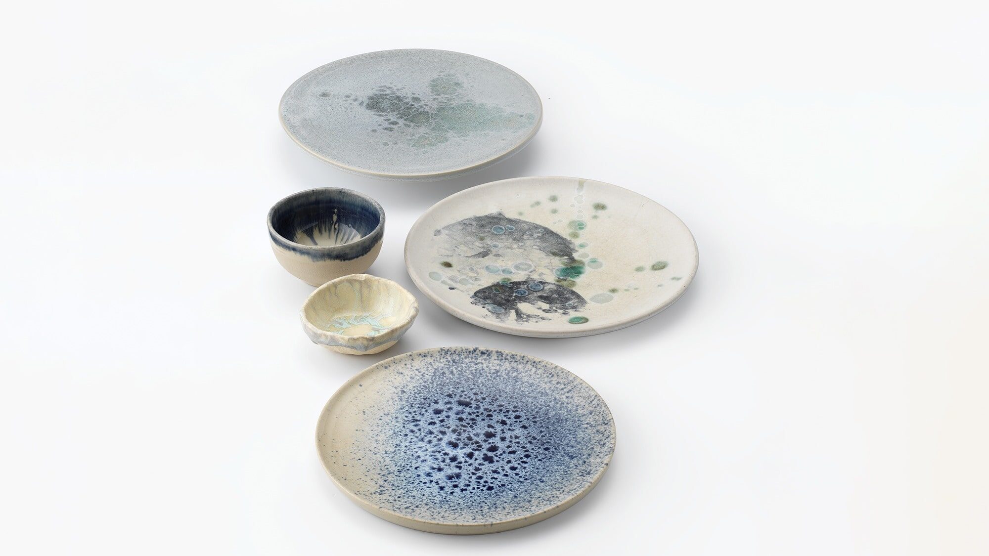 Five ceramic dishes and cups with abstract blue, green, and gray glaze patterns—your Fave Five Little Escapes—arranged on a white background.