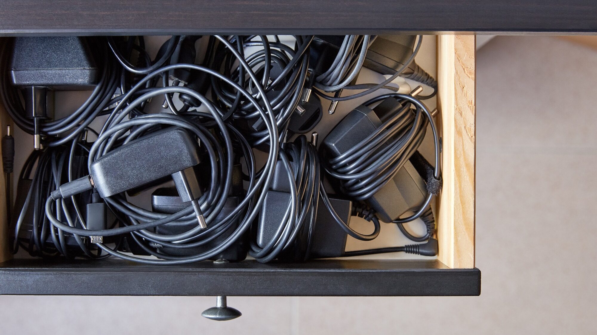 Drawer filled with tangled black cords, cables, and power adapters.