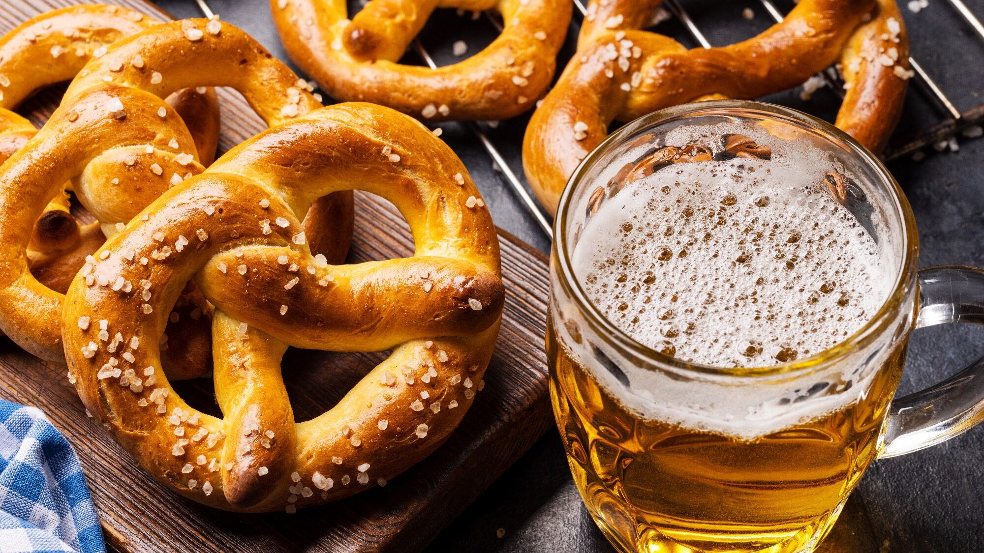A glass mug of beer sits next to several salted soft pretzels on a wooden board.