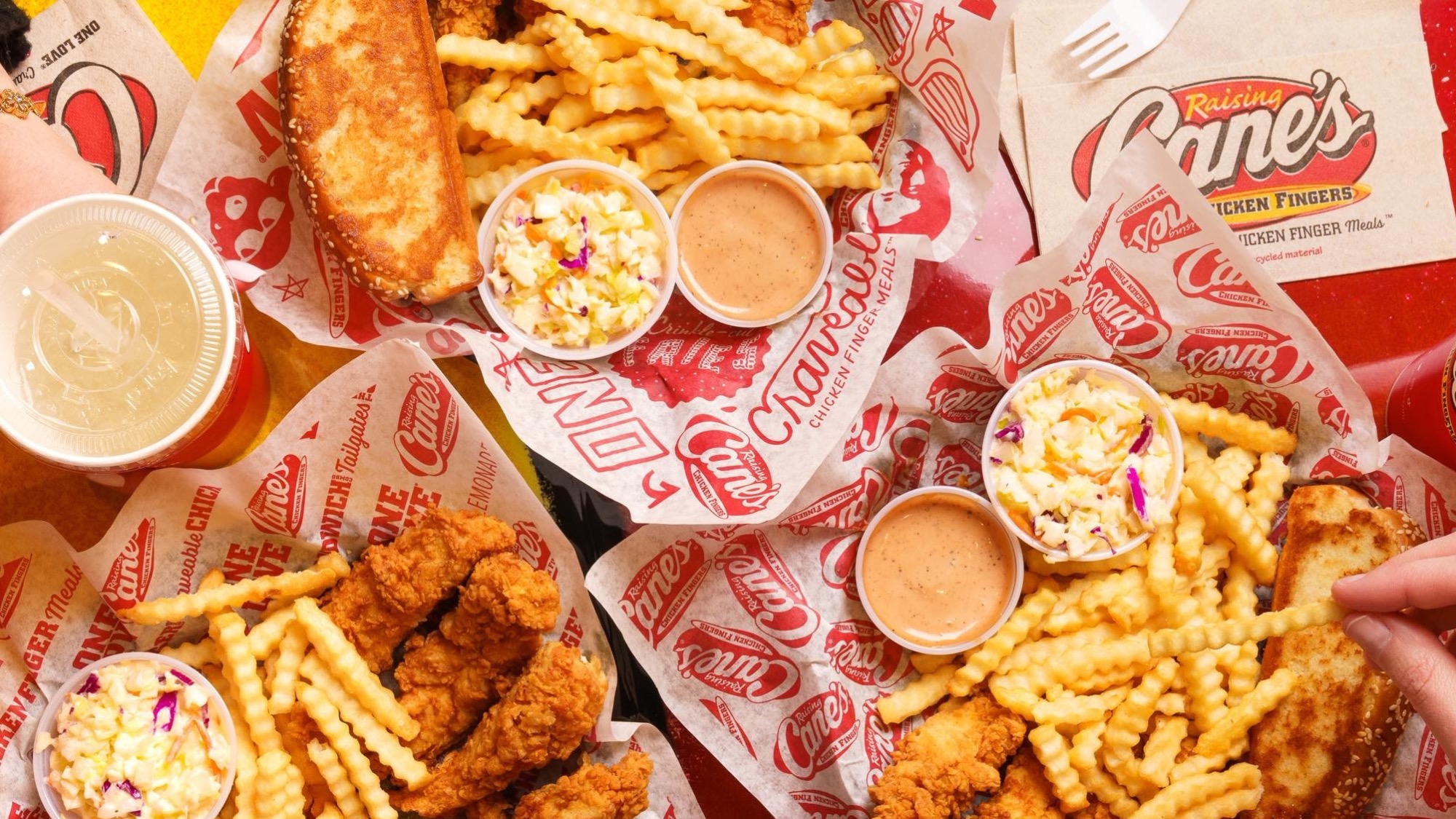Three meals of fried chicken fingers, crinkle-cut fries, coleslaw, toast, sauce cups, and drinks on Raising Cane’s branded paper.