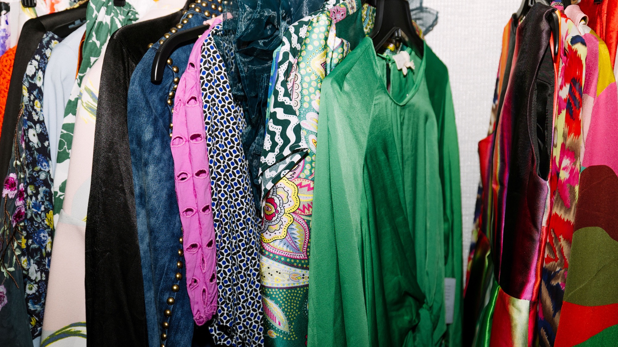 A rack of colorful, assorted clothing including dresses, shirts, and jackets in various patterns and fabrics hanging on black hangers.